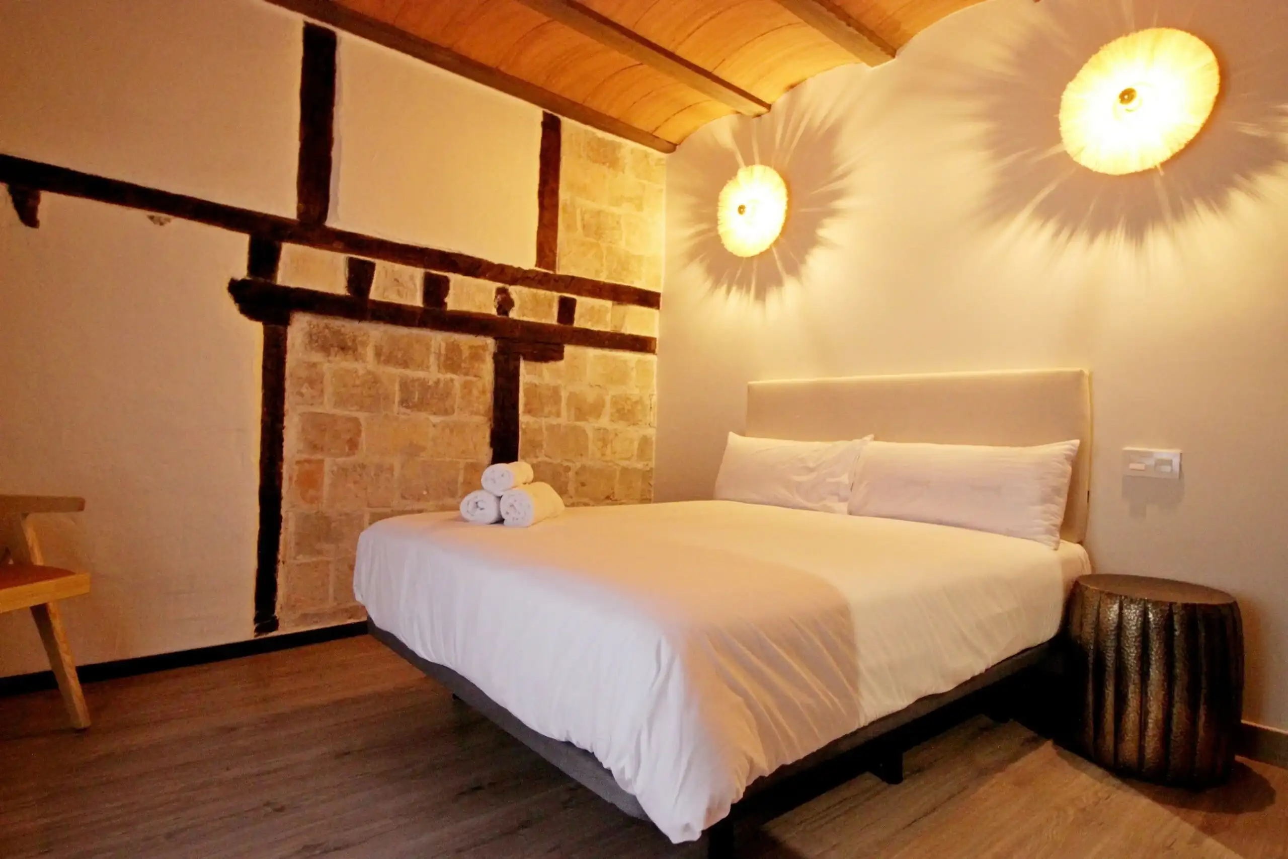 Dormitorio acogedor en El Patio de los Ángeles, con cama doble, paredes de piedra y vigas de madera, iluminación cálida y decoración rústica, ideal para una estancia relajante en un apartamento con encanto en el centro histórico de Teledo.
